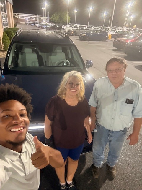 Damarion celebrating a nighttime vehicle delivery with two customers